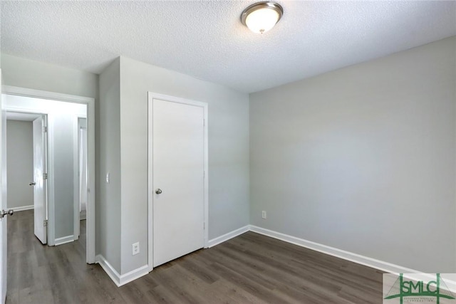 unfurnished bedroom with baseboards, a textured ceiling, dark wood-style floors, and a closet