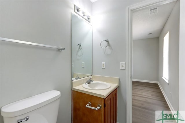 bathroom with vanity, toilet, baseboards, visible vents, and wood finished floors