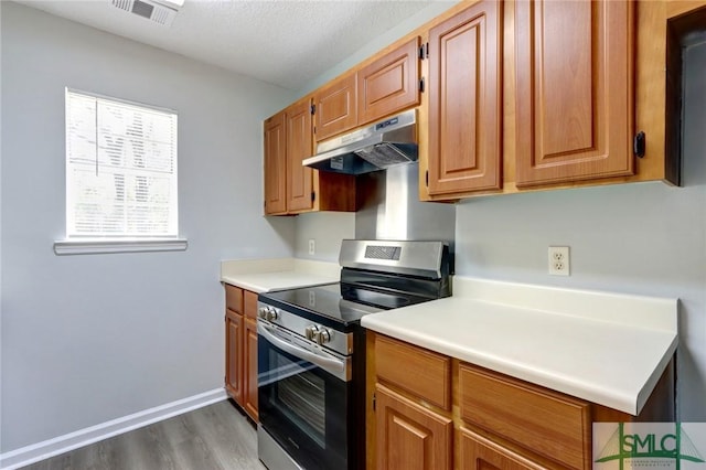 kitchen featuring light countertops, under cabinet range hood, stainless steel electric stove, visible vents, and wood finished floors