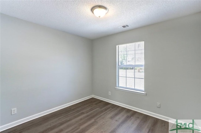 unfurnished room with baseboards, dark wood-style flooring, a textured ceiling, and visible vents