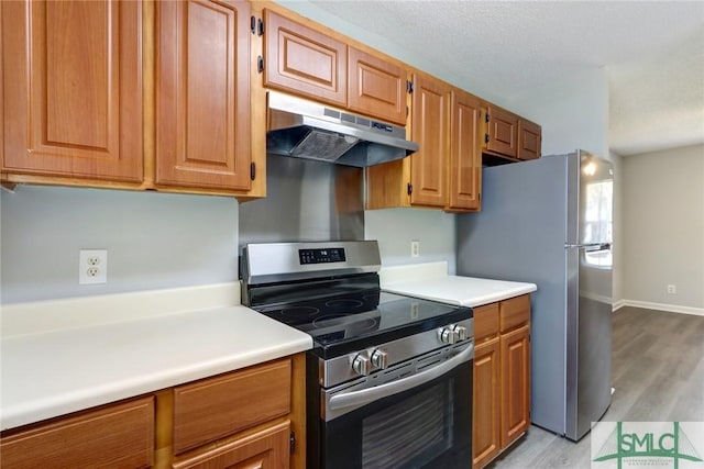 kitchen with light countertops, appliances with stainless steel finishes, brown cabinets, under cabinet range hood, and light wood-style floors