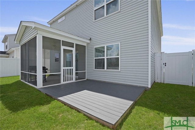 back of house featuring a deck, a sunroom, a fenced backyard, and a lawn