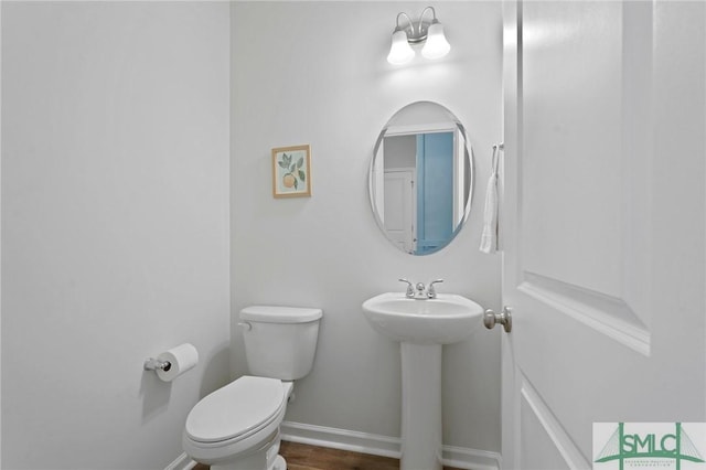 half bath featuring wood finished floors, baseboards, and toilet
