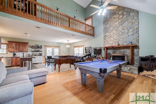 rec room with a towering ceiling, a stone fireplace, billiards, light wood-style flooring, and ceiling fan