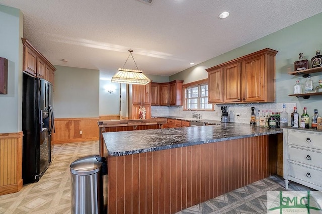 kitchen featuring black fridge with ice dispenser, a sink, a peninsula, brown cabinets, and wainscoting