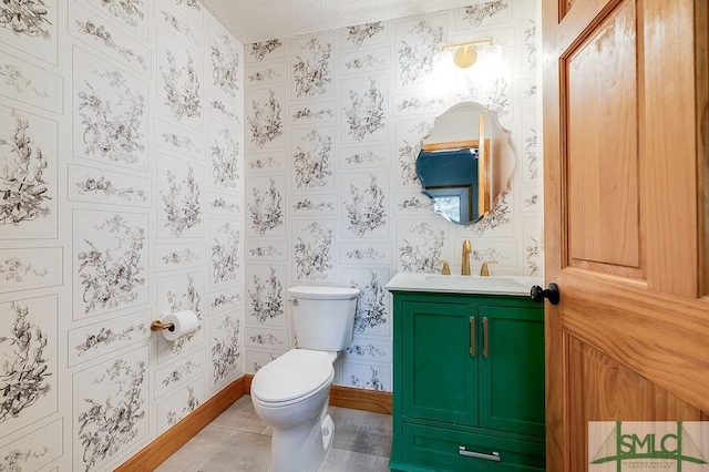 half bath featuring a textured ceiling, baseboards, wallpapered walls, toilet, and vanity