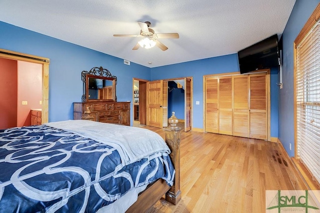 bedroom with a ceiling fan, a textured ceiling, multiple closets, baseboards, and light wood-style floors