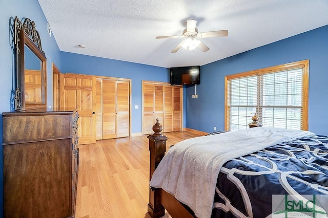 bedroom with a textured ceiling, light wood-type flooring, baseboards, two closets, and ceiling fan