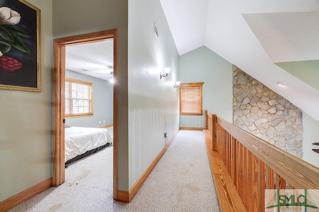 hall with light carpet, baseboards, visible vents, and vaulted ceiling