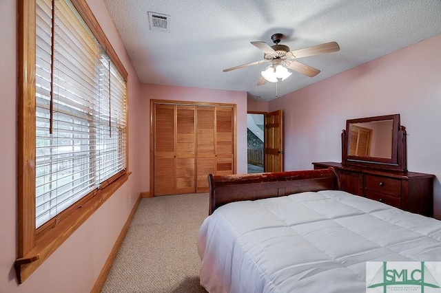 bedroom with a closet, light carpet, a textured ceiling, baseboards, and visible vents