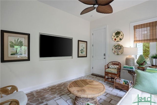 sitting room featuring stone finish flooring, baseboards, and a ceiling fan