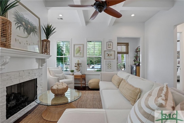 living area with a ceiling fan, visible vents, a stone fireplace, wood finished floors, and beam ceiling