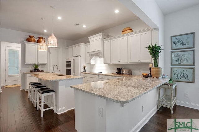 kitchen with dark wood-style flooring, high end fridge, white cabinets, under cabinet range hood, and a breakfast bar area
