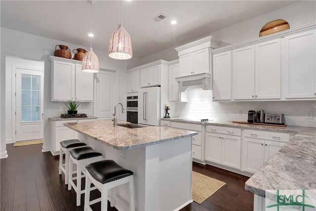 kitchen with visible vents, white cabinets, a sink, under cabinet range hood, and high end fridge