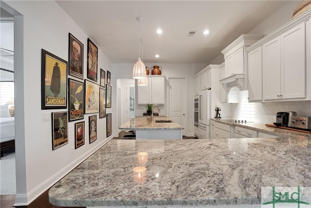 kitchen with light stone counters, high end white fridge, an island with sink, white cabinetry, and a sink