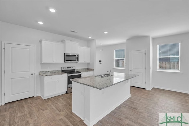 kitchen featuring appliances with stainless steel finishes, a kitchen island with sink, white cabinetry, light stone countertops, and light wood-style flooring