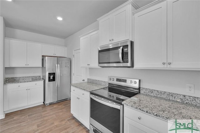 kitchen with stainless steel appliances, white cabinets, light stone counters, and light wood-style flooring