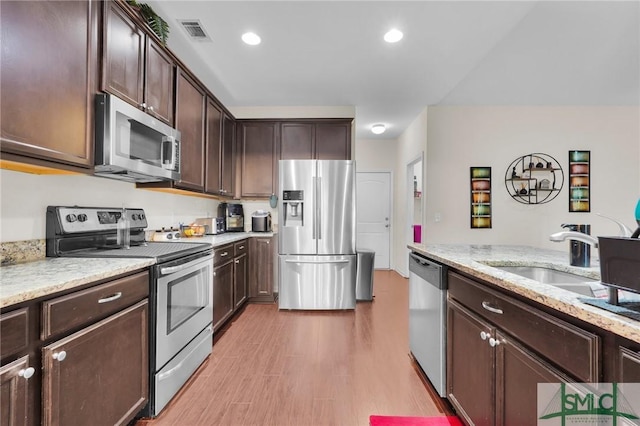 kitchen featuring dark brown cabinetry, visible vents, stainless steel appliances, light wood finished floors, and a sink
