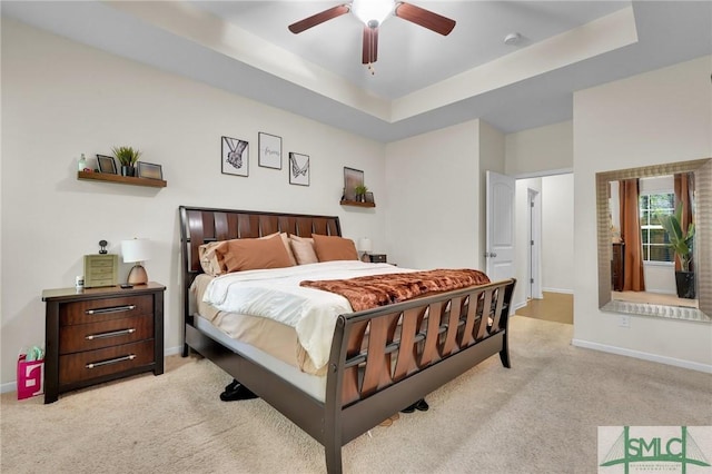 bedroom featuring light carpet, ceiling fan, baseboards, and a raised ceiling