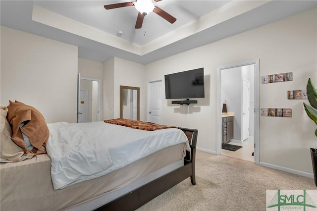 bedroom with baseboards, light carpet, ensuite bathroom, a ceiling fan, and a raised ceiling