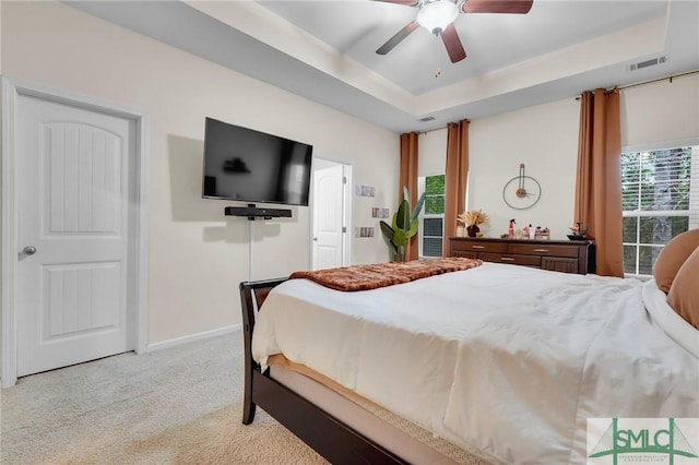 bedroom with baseboards, light carpet, visible vents, a tray ceiling, and ceiling fan