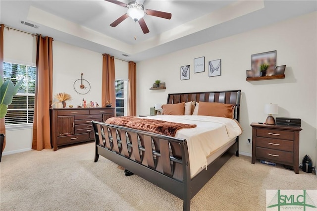 bedroom featuring ceiling fan, a tray ceiling, light colored carpet, visible vents, and baseboards