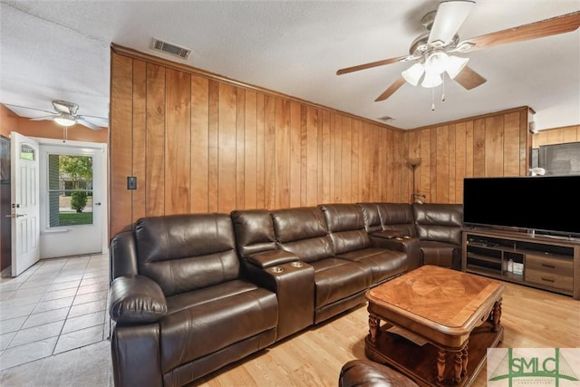 living area with a textured ceiling, a ceiling fan, visible vents, wood walls, and light wood finished floors