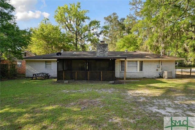 back of house featuring a sunroom, a yard, a chimney, cooling unit, and brick siding