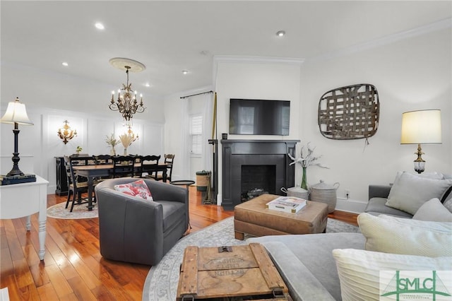 living area featuring crown molding, wood finished floors, a chandelier, a tiled fireplace, and recessed lighting