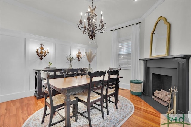 dining area featuring a chandelier, ornamental molding, light wood-type flooring, and a fireplace with flush hearth