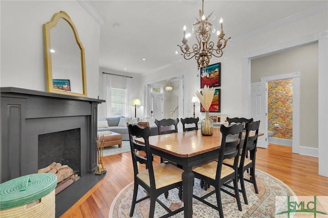 dining area with light wood-style floors, crown molding, a fireplace, baseboards, and a chandelier