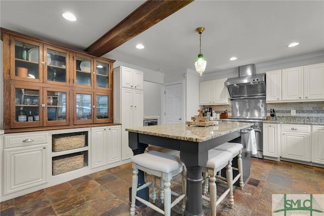 kitchen featuring stone tile floors, wall chimney exhaust hood, glass insert cabinets, backsplash, and recessed lighting