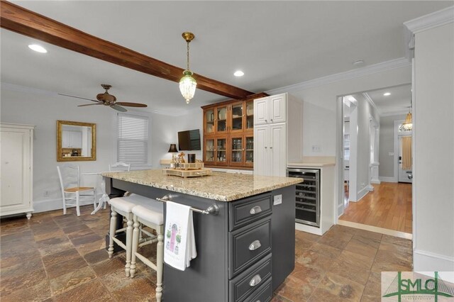 kitchen featuring wine cooler, stone tile flooring, baseboards, crown molding, and beam ceiling