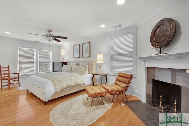 bedroom with wood finished floors, recessed lighting, crown molding, baseboards, and a tiled fireplace