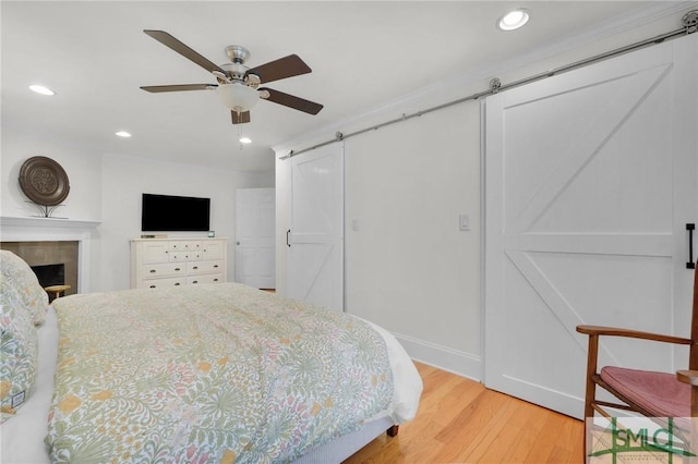 bedroom featuring wood finished floors, a barn door, recessed lighting, a fireplace, and ceiling fan
