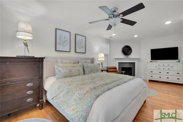 bedroom featuring wood finished floors, ornamental molding, recessed lighting, a fireplace, and a ceiling fan