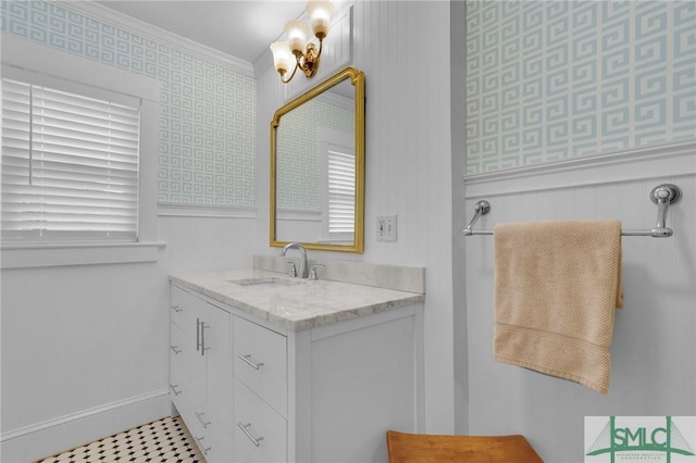bathroom featuring wallpapered walls, vanity, crown molding, baseboards, and a wainscoted wall