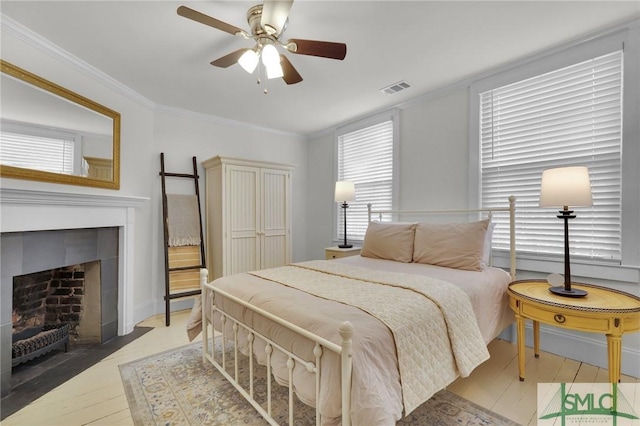 bedroom with multiple windows, crown molding, wood finished floors, a tile fireplace, and a ceiling fan