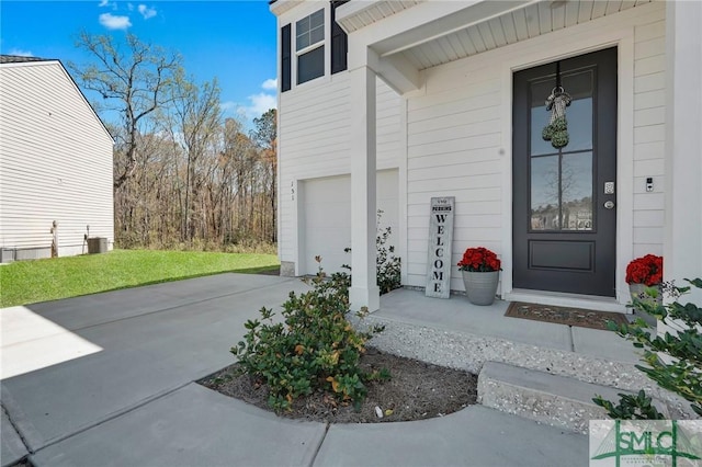 doorway to property featuring an attached garage, concrete driveway, and central AC unit
