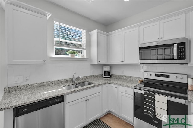 kitchen with tasteful backsplash, a sink, white cabinetry, light stone countertops, and stainless steel appliances