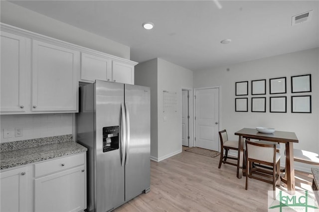 kitchen with light wood-type flooring, stainless steel fridge, backsplash, white cabinets, and visible vents