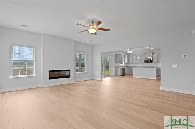 unfurnished living room featuring light wood-style flooring, a wealth of natural light, a ceiling fan, and baseboards