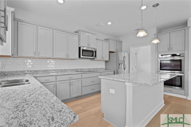 kitchen with a sink, backsplash, light wood-style flooring, and appliances with stainless steel finishes