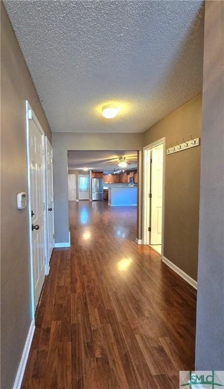 hallway with baseboards, a textured ceiling, and wood finished floors