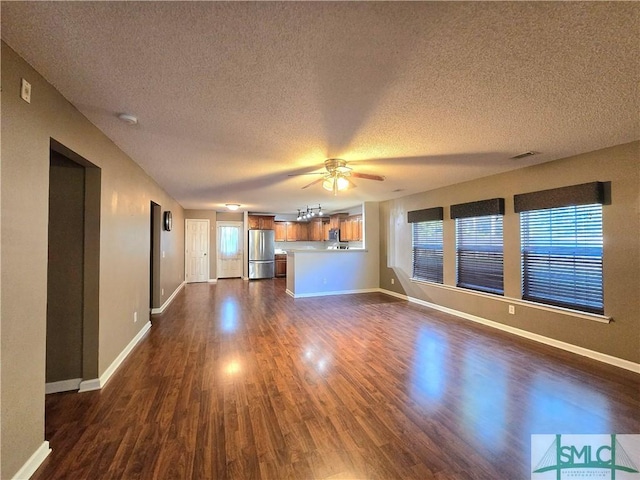 unfurnished living room featuring visible vents, baseboards, ceiling fan, a textured ceiling, and dark wood-style floors