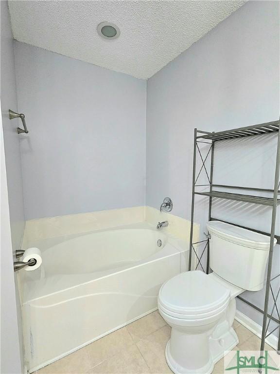 bathroom featuring tile patterned flooring, a bath, a textured ceiling, and toilet