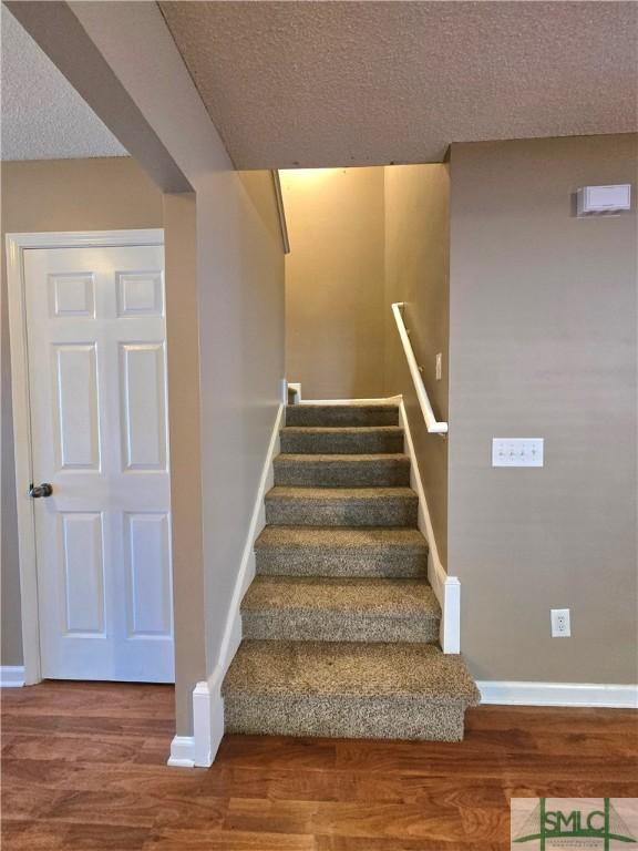 staircase with a textured ceiling, wood finished floors, and baseboards