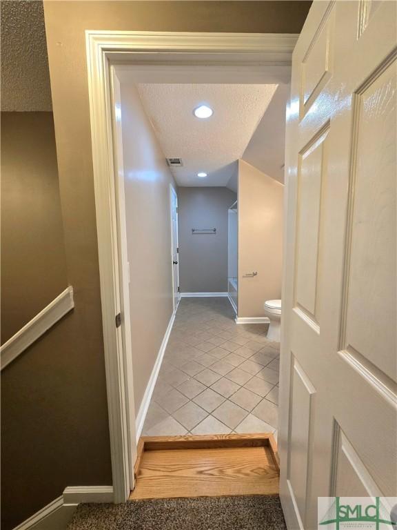 hall with visible vents, baseboards, light tile patterned flooring, and a textured ceiling