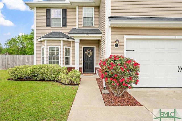 entrance to property with an attached garage, fence, and a lawn