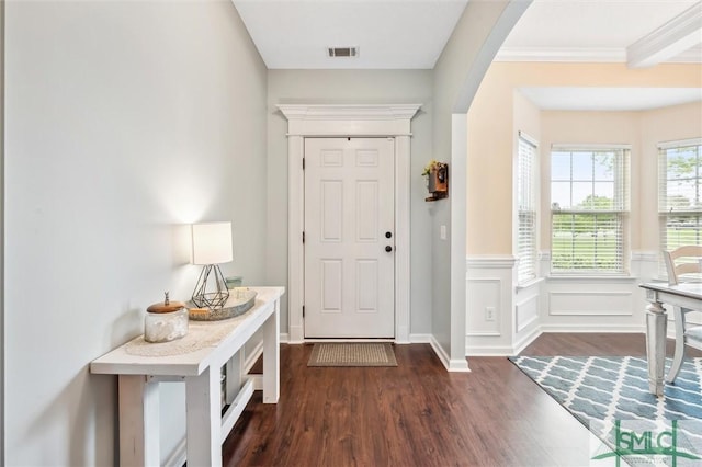 foyer with ornamental molding, dark wood-style floors, wainscoting, visible vents, and arched walkways